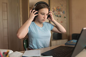 Girl with headphones on staring at laptop screen