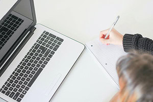 Overhead view of woman writing on paper near open laptop