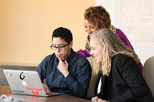 Women looking at laptop screen with site design on white board behind them