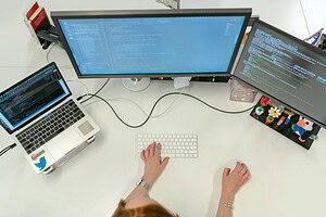 Overhead view of woman at computer workstation with two monitors and laptop