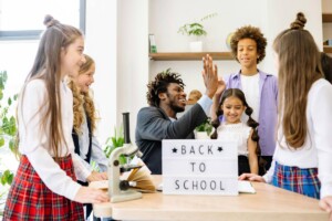 Teacher with boy and girl students giving a high five to a student behind back to school sign