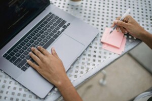 Overhead view of hands on a laptop keyboard and taking notes on a post it note