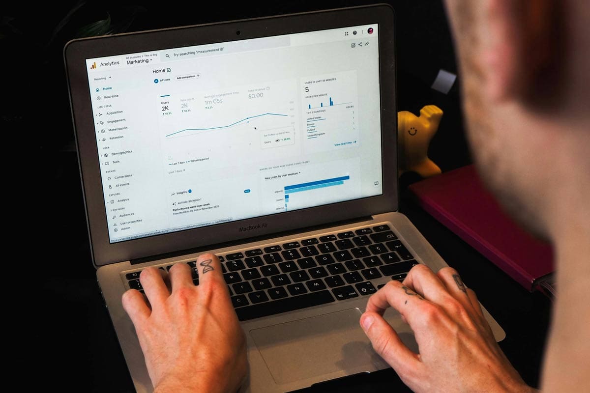 View of man with finger tattoos typing on a macbook keyboard looking at Google Analytics on the screen