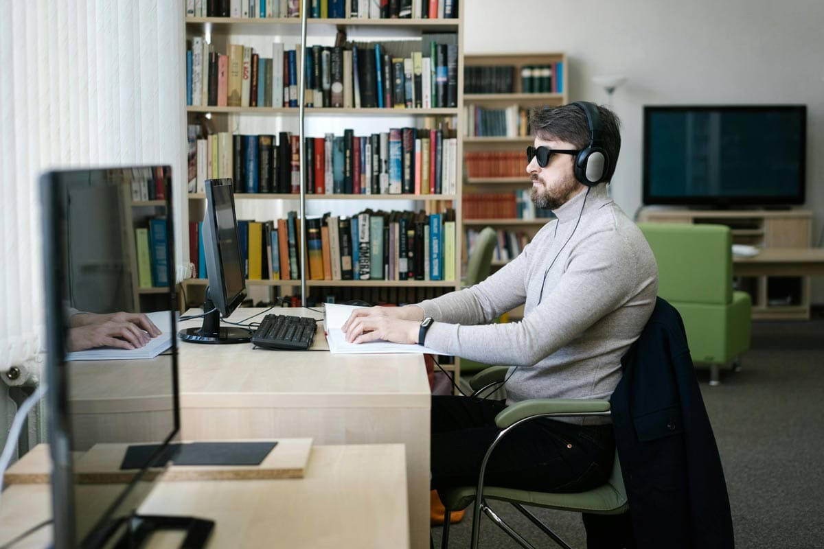 Blind man at desk wearing headphones using braille in front of a computer